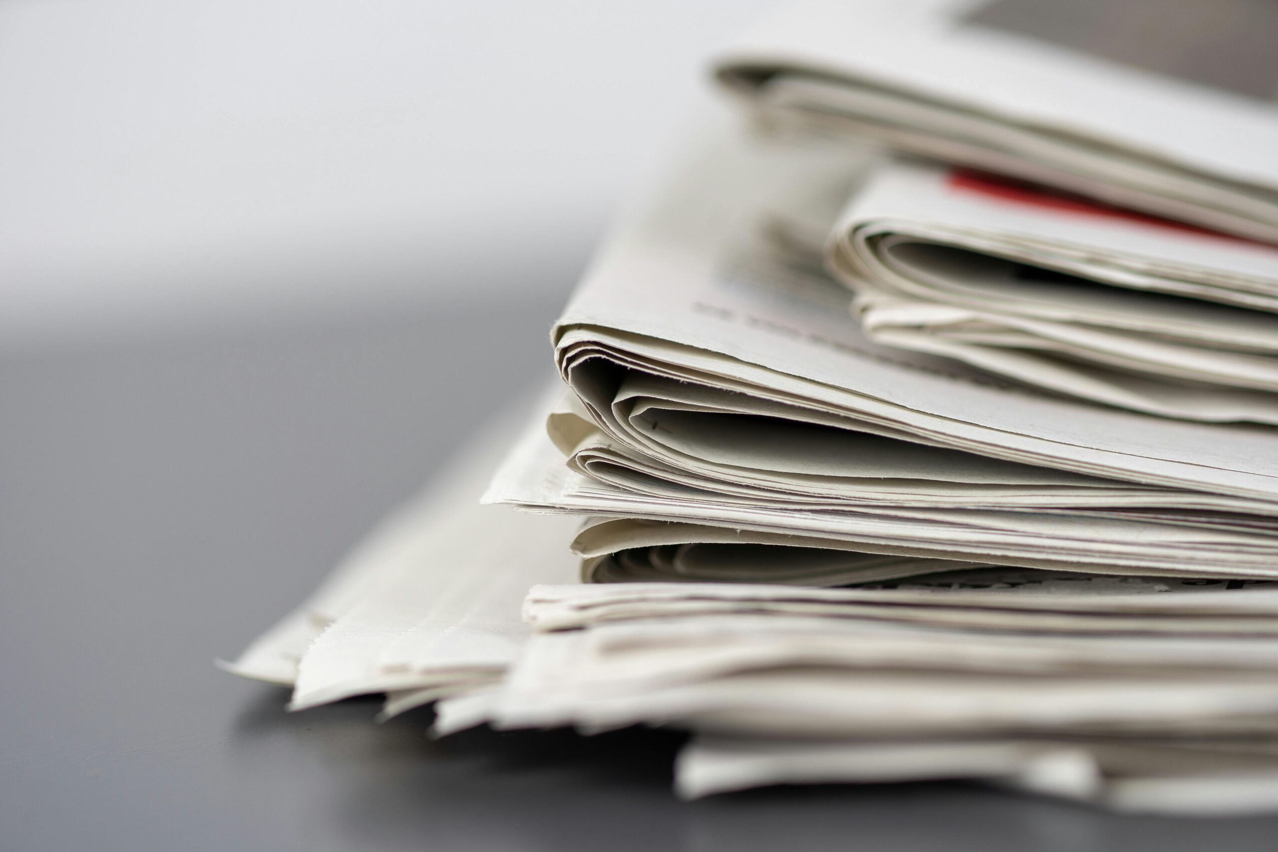 Close-up of stacked newspapers on a table, representing media and journalism.